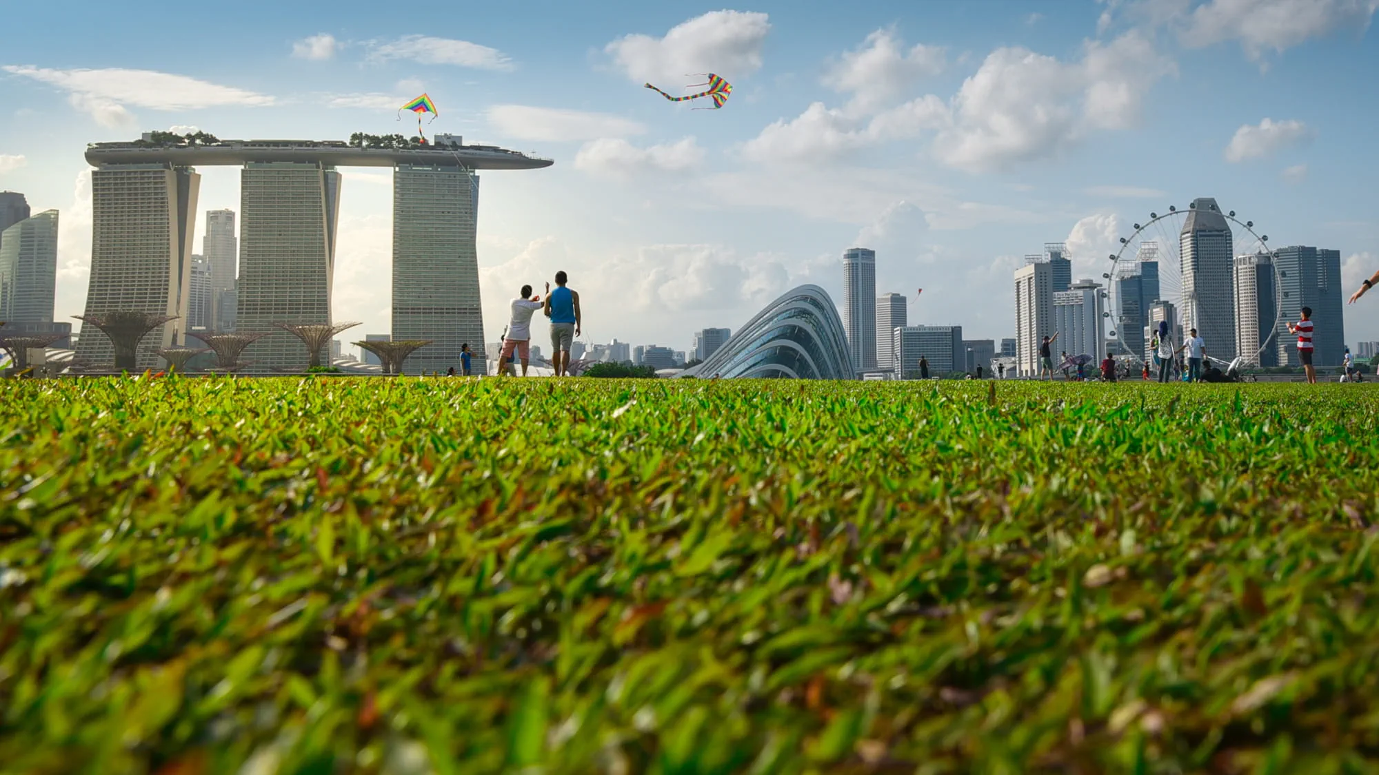 Adults and children playing with a kite in the green parks surrounding Marina Bay area in Singapore on a sunny day