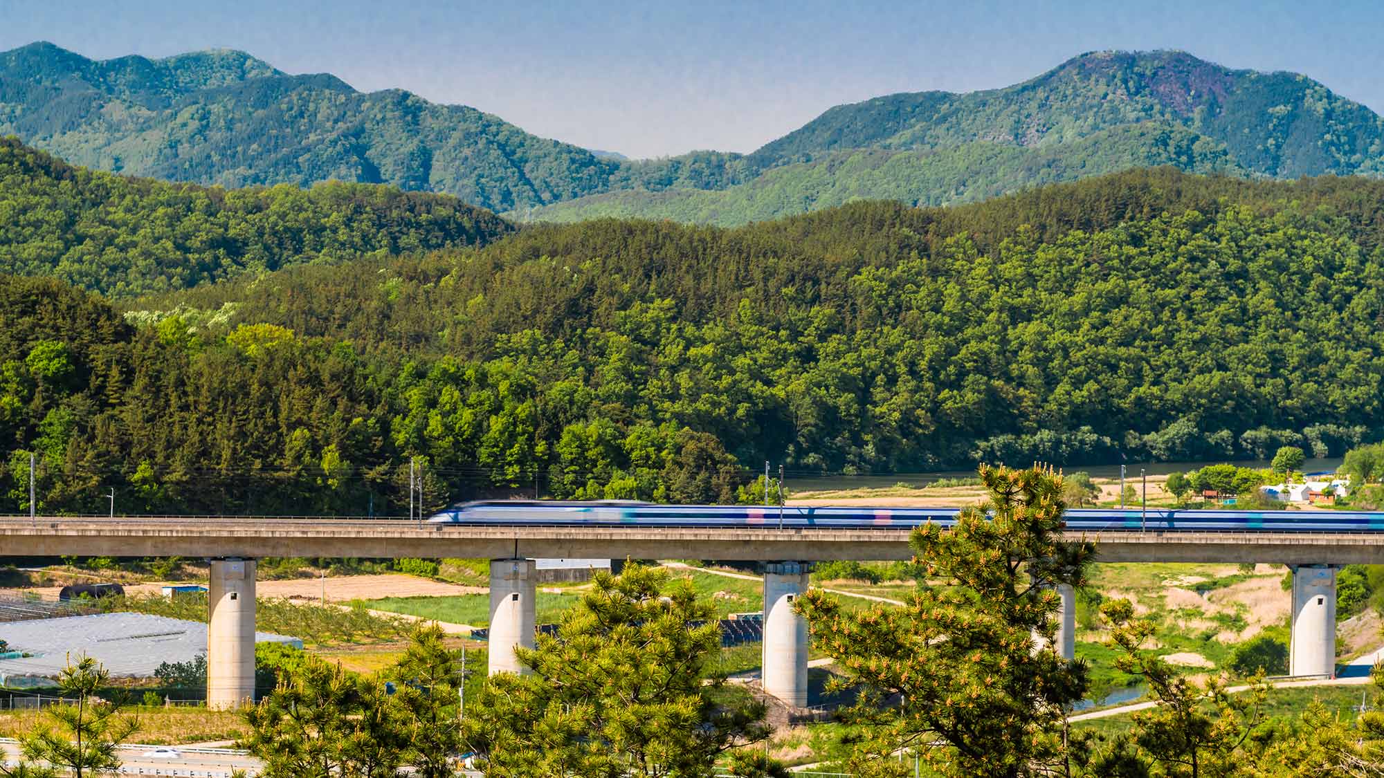 High speed train speeding across concrete railroad bridge in rural countryside