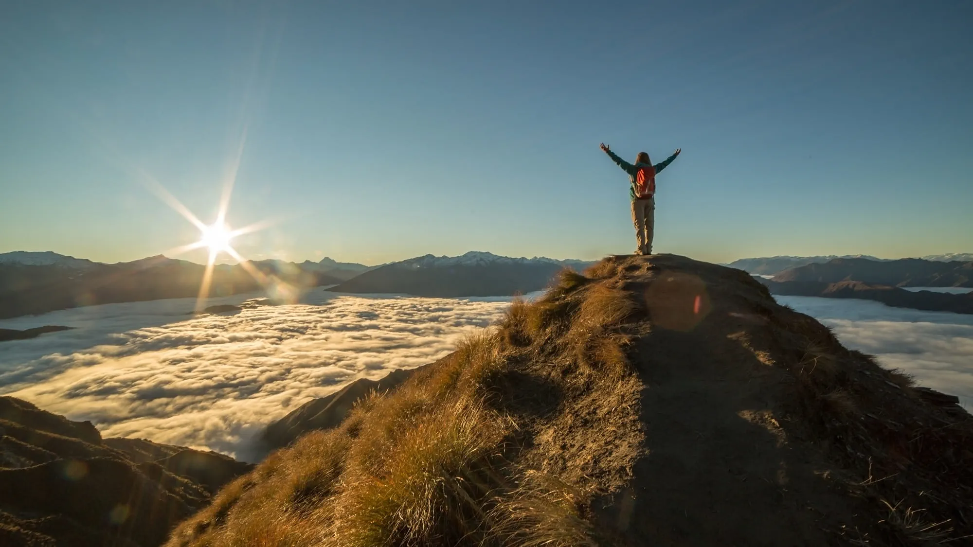 A person standing on top of a mountain in new Zealand surrounded by clouds