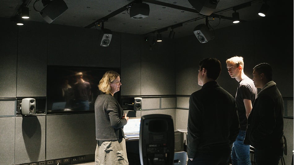 A woman and three men standing and talking in a SoundLab: a room with several speakers and lights fitted to the walls and ceilings