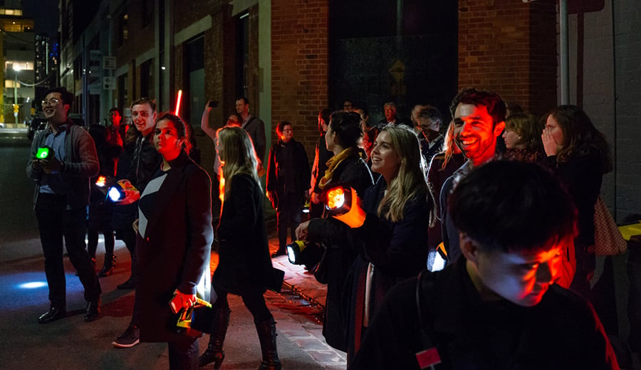 A group of people holding torches in a dark city street at night time experiencing lighting techniques