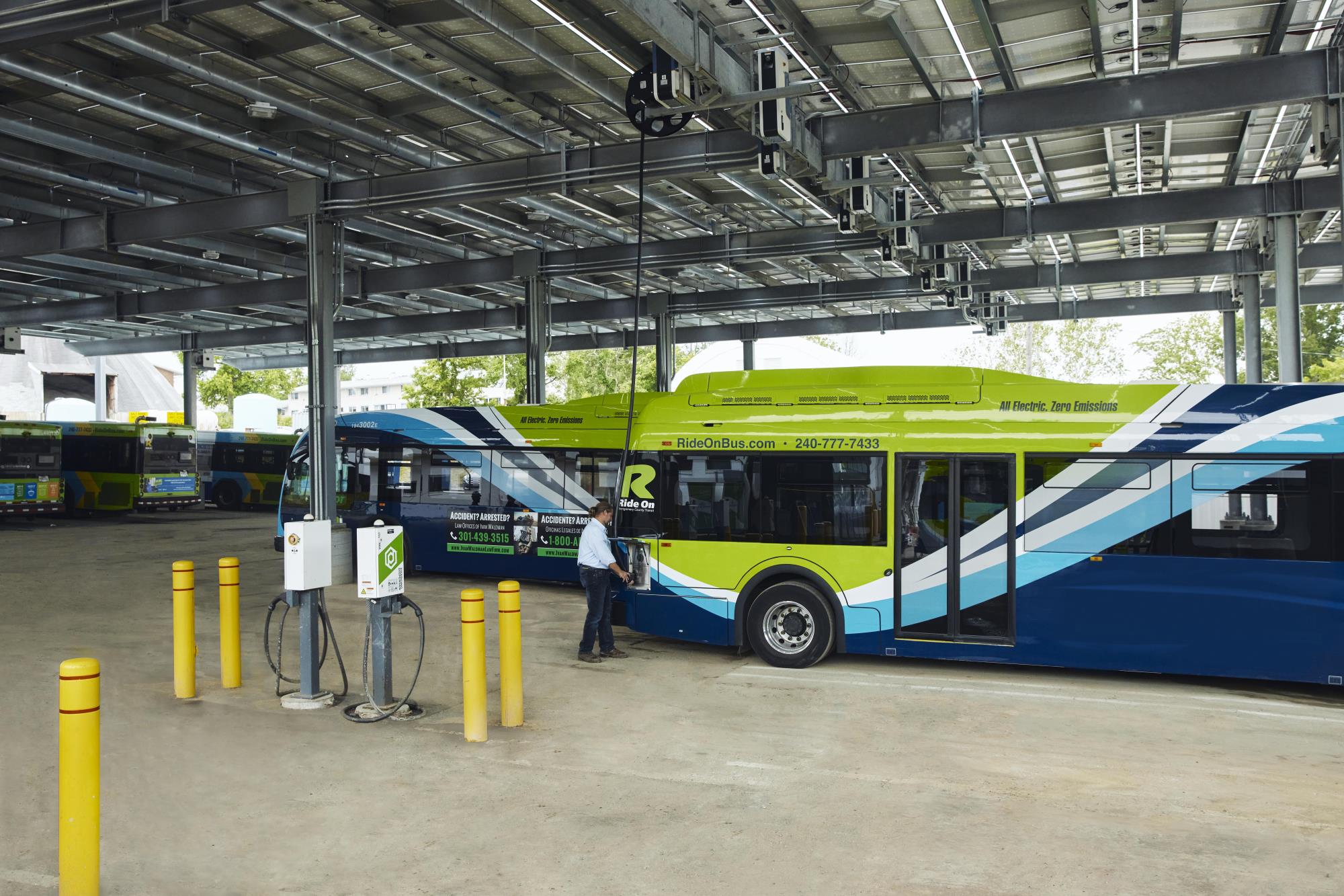 A covered bus depot with electric bus chargers and green and blue EV busses