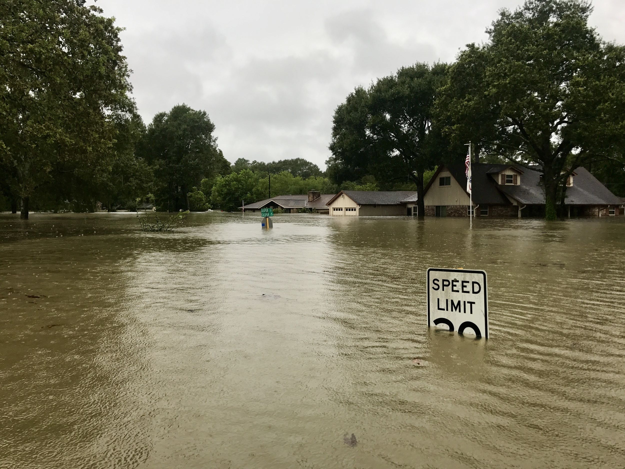 Photo of a flooded community, with water up high enough to almost reach top of street sign. 