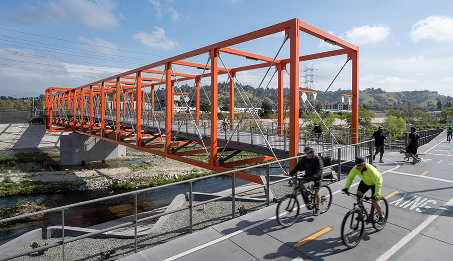 A bright orange bridge with bicyclists passing by. 