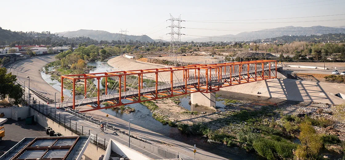 A bright orange bridge spanning the LA River with a cyclist in the bottom left corner.