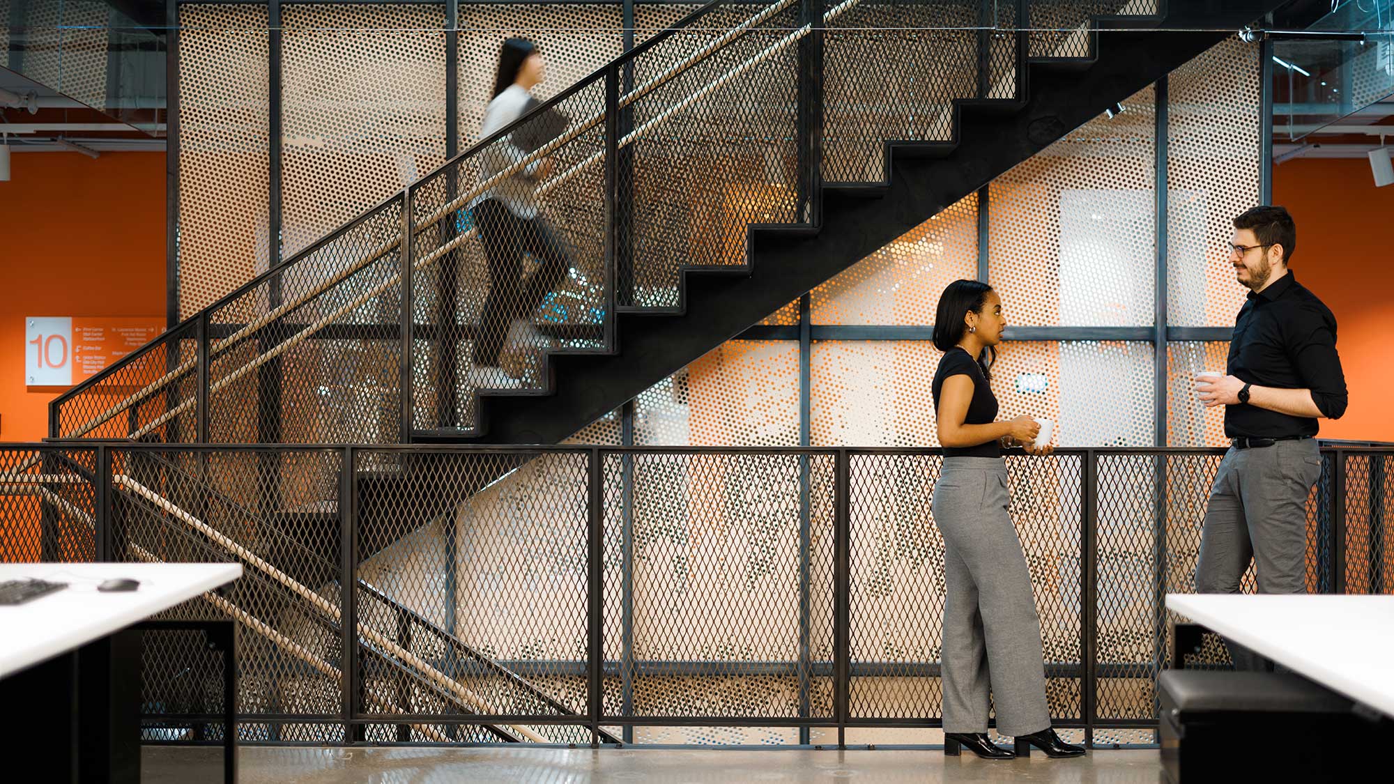 Two people talking in front of a staircase in an office