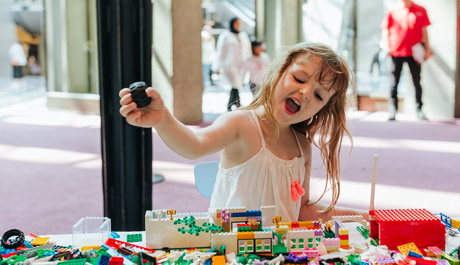 A young girl playing and having fun with LEGO coloured bricks at a table full of pieces