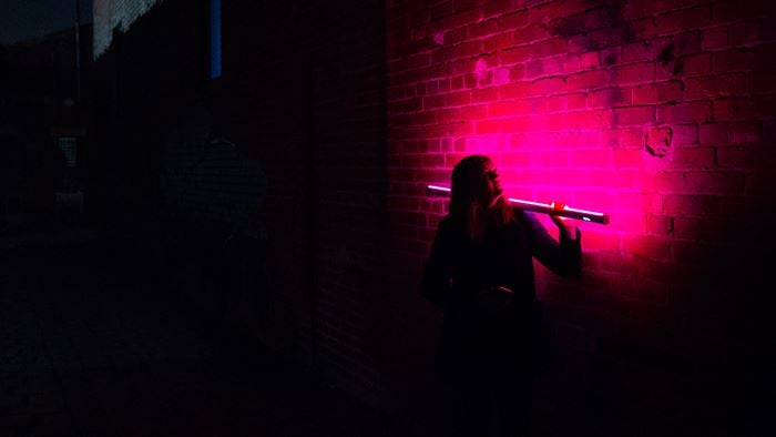 Dark alley at night with woman holding up pink strip lighting