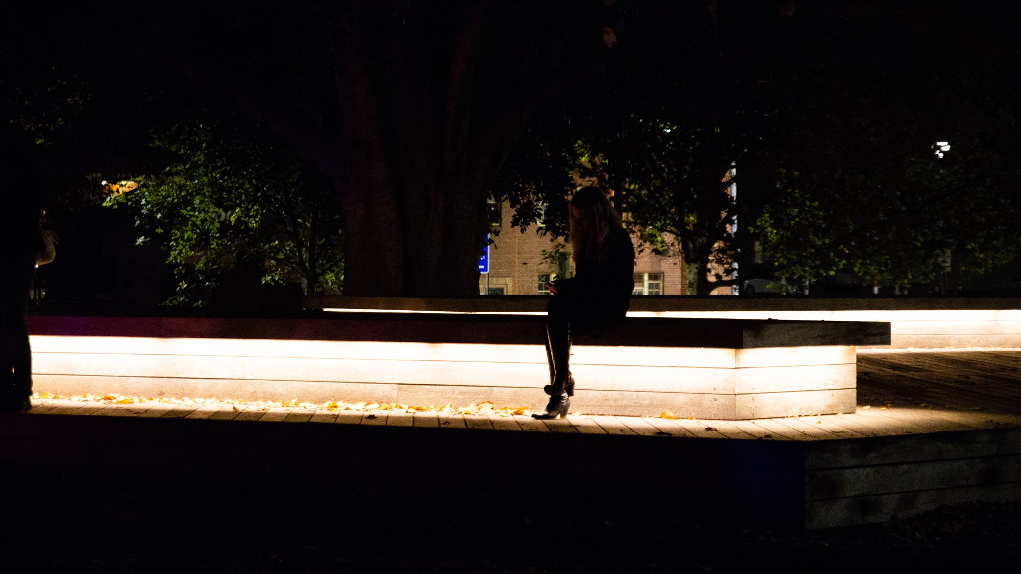 Woman sitting on a seat in the city at nighttime, with subdued lighting under and around seating