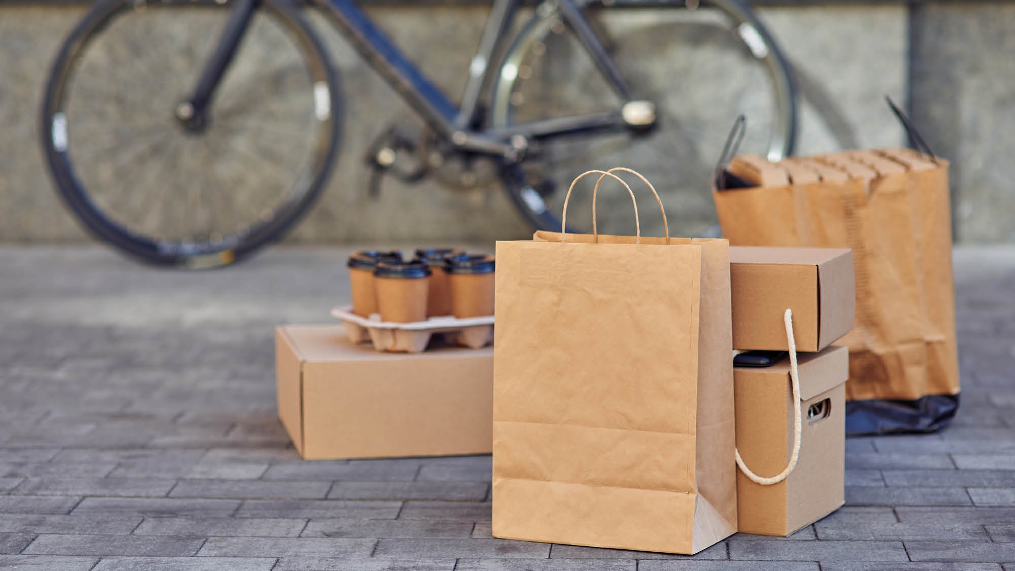 Brown shopping bags, boxes, takeaway coffee cups, delivered to a street. Online shopping.