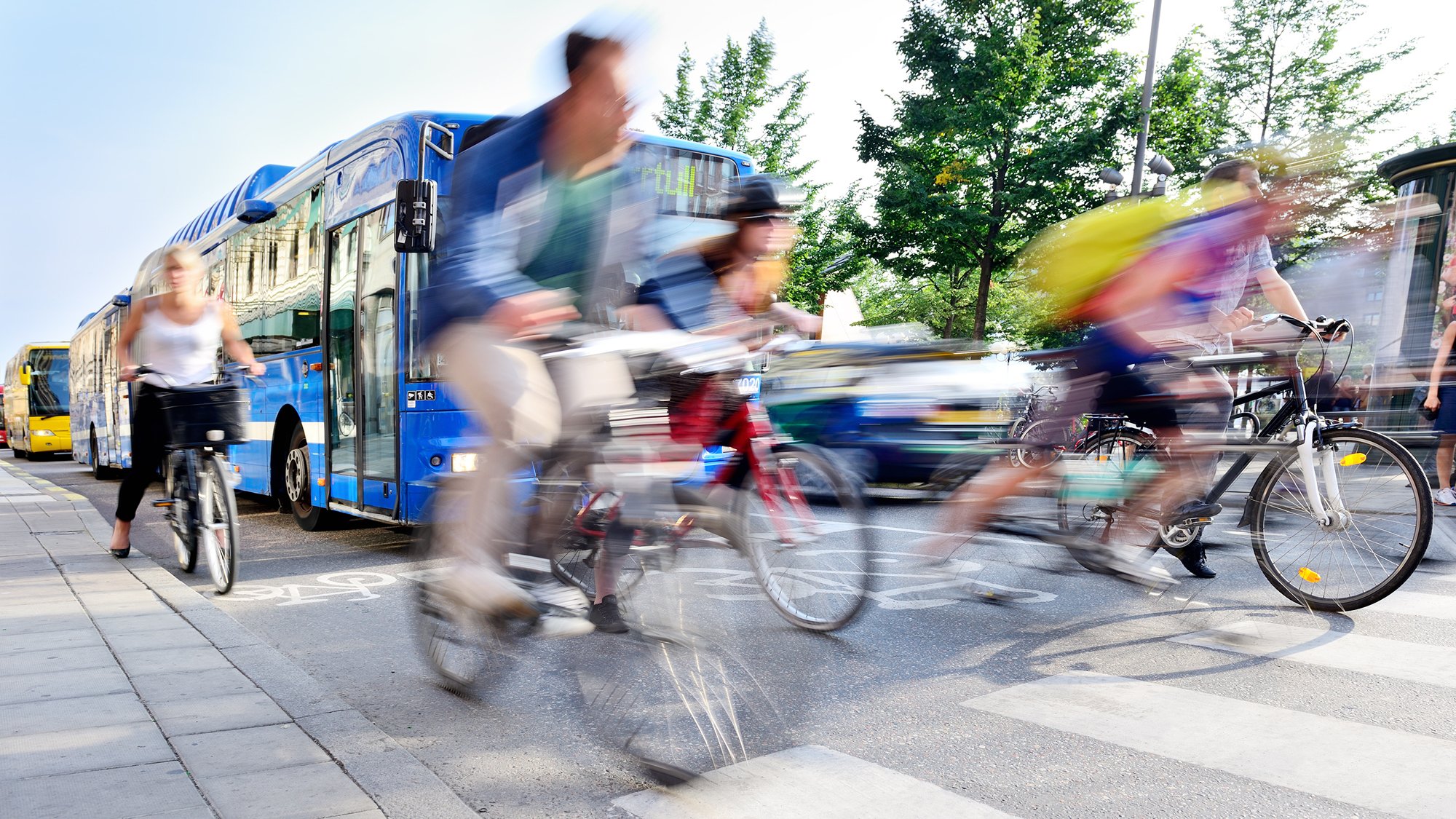 A blurred image of people riding bikes in front of a row of buses on a sunny day