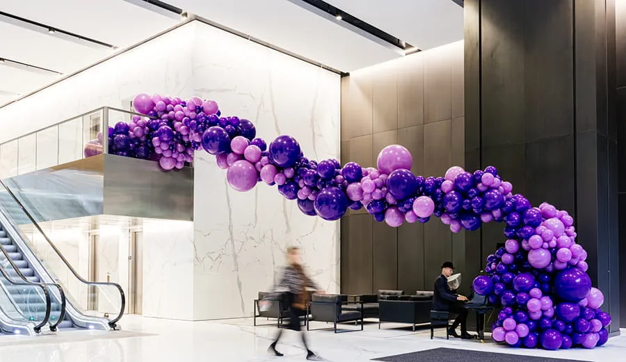 Lobby entrance with high ceilings, escalator, marble walls, piano, and a large sculpture of purple floating balloons