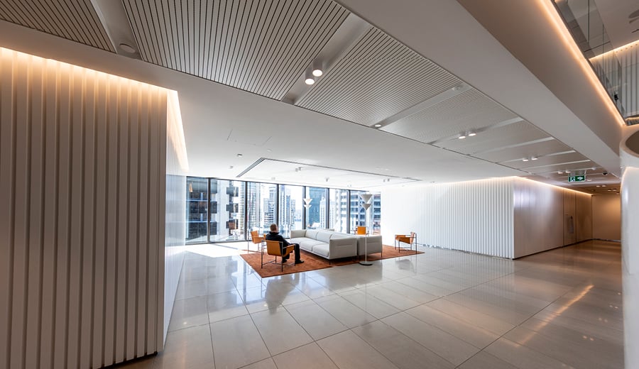 A large space with sofas and carpets, modern lighting and ceiling to floor windows inside an office tower