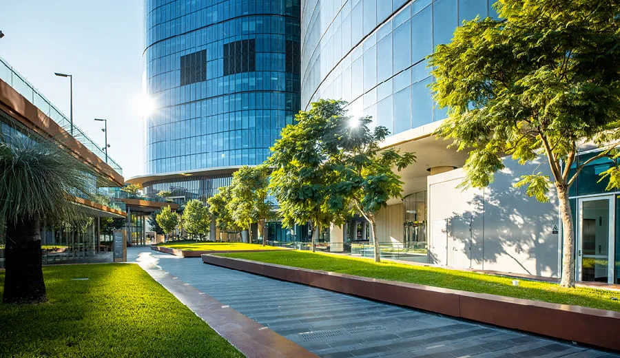 Entrance level to an office tower with pathways, garden beds and grass at day time