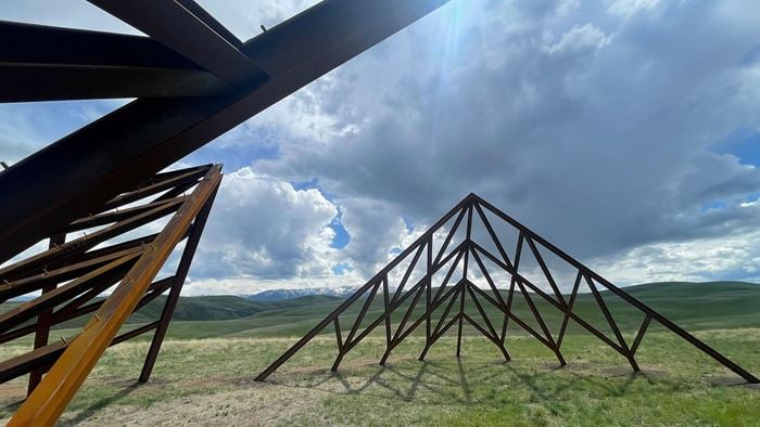 Metal pyramid structures in a field with clouds above and mountains in the distance