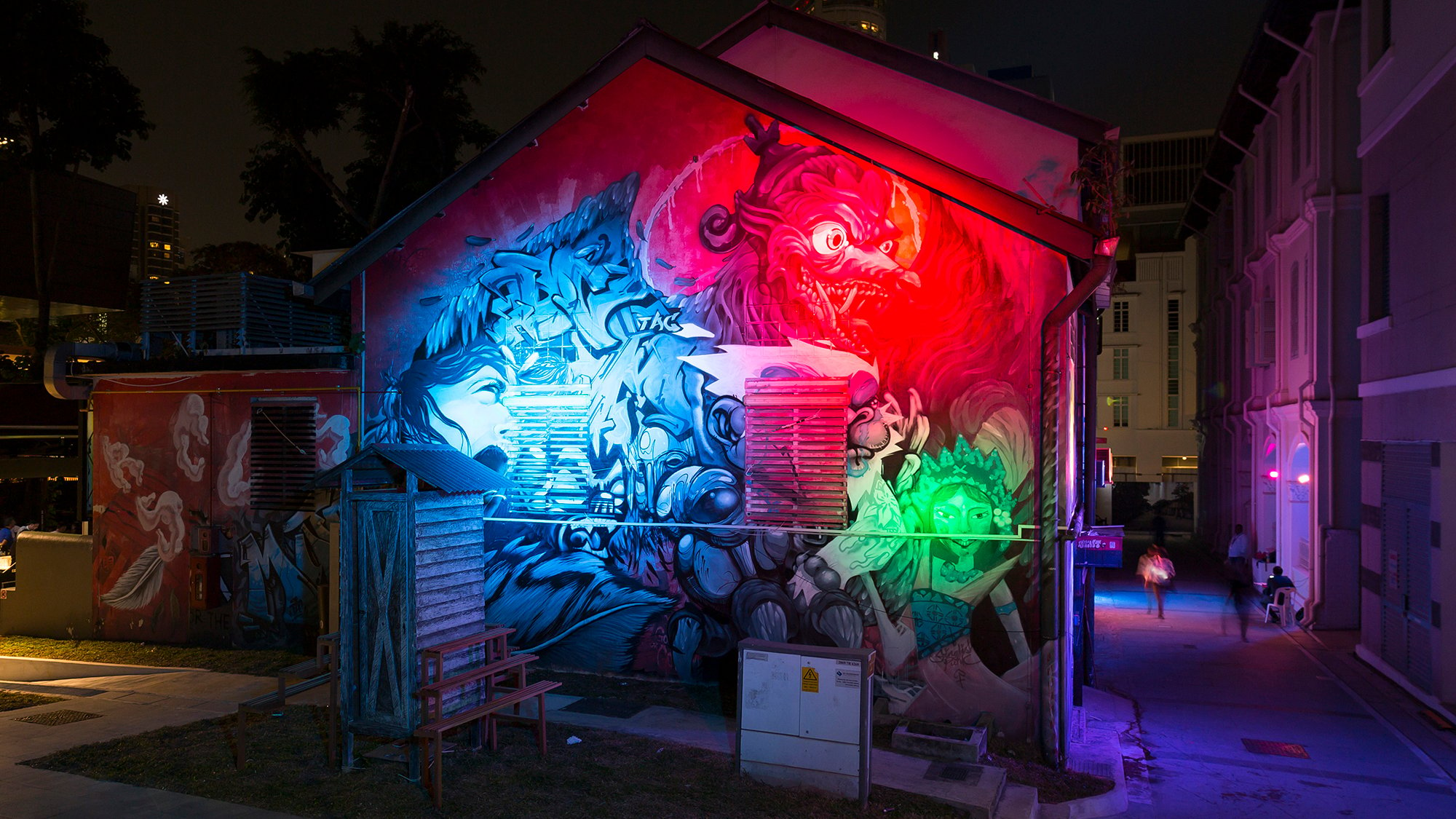 Night photo taken of the corner of a building covered in graffiti and lit up by coloured spotlights