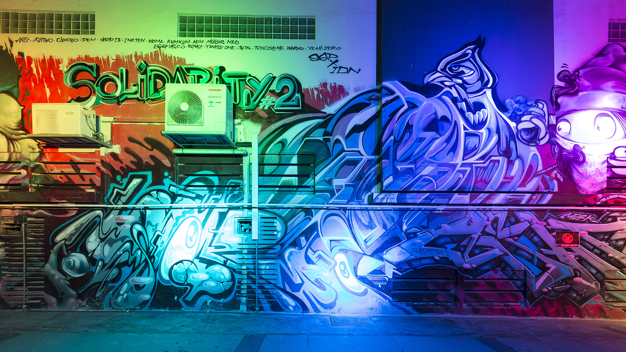 A graffiti covered wall at night lit up by coloured spotlights
