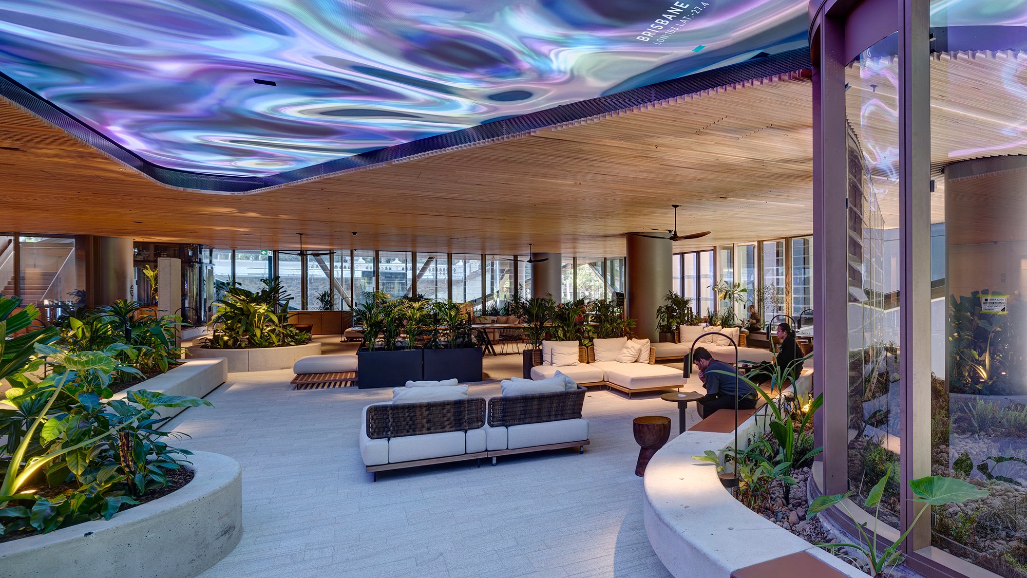 Modern office space with curved garden beds with plants, adaptable seating, open space, natural air, glass facade and a decorative LED display ceiling