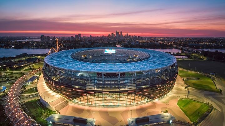 Optus Stadium at night with a pink sunset in the background