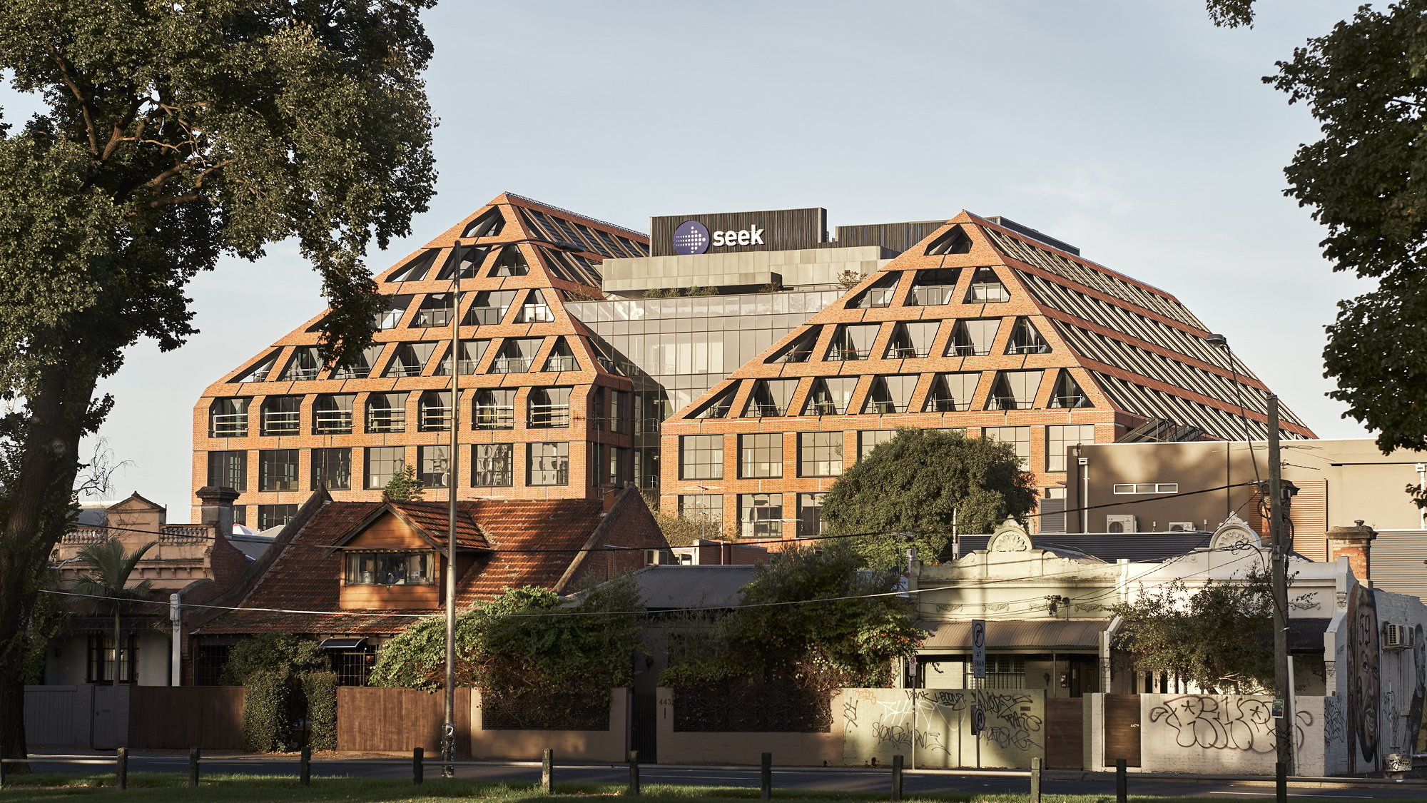A multi-floor building with triangular shaped facades, timber beams, roof top gardens and brick work