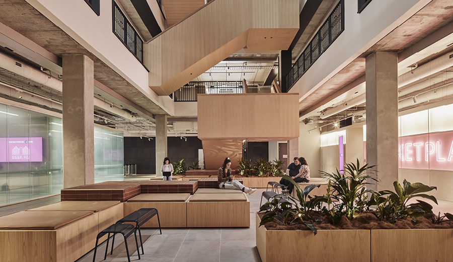 Ground floor space with timber seating, plants and a timber staircase going up through open floor plates