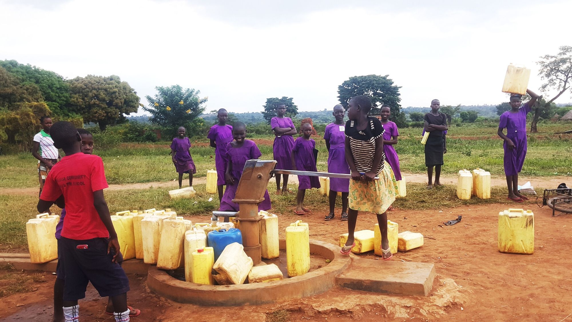 People using a handpump for water in Uganda, with containers lined up to fill with water.