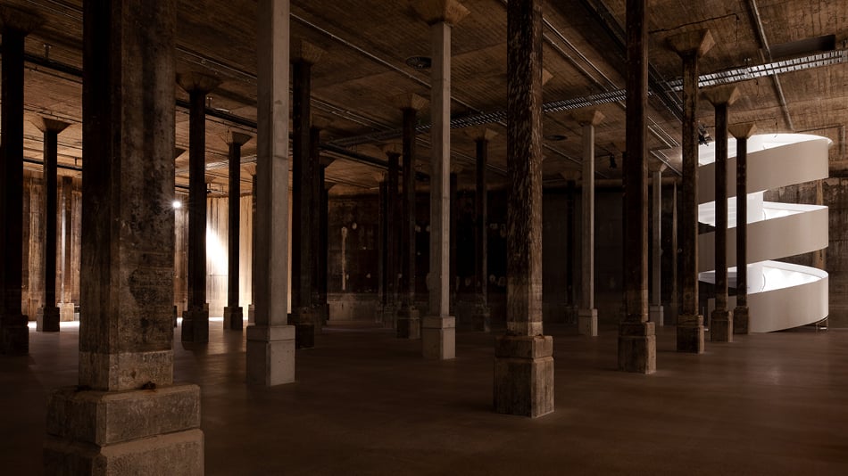Inside a dark, cavernous room with pillars and a white, swirling staircase
