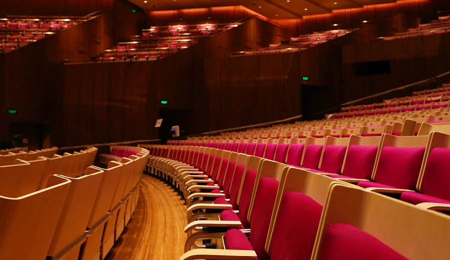 Sideway view looking at rows of empty seats with red cushions and timber backs inside a concert hall