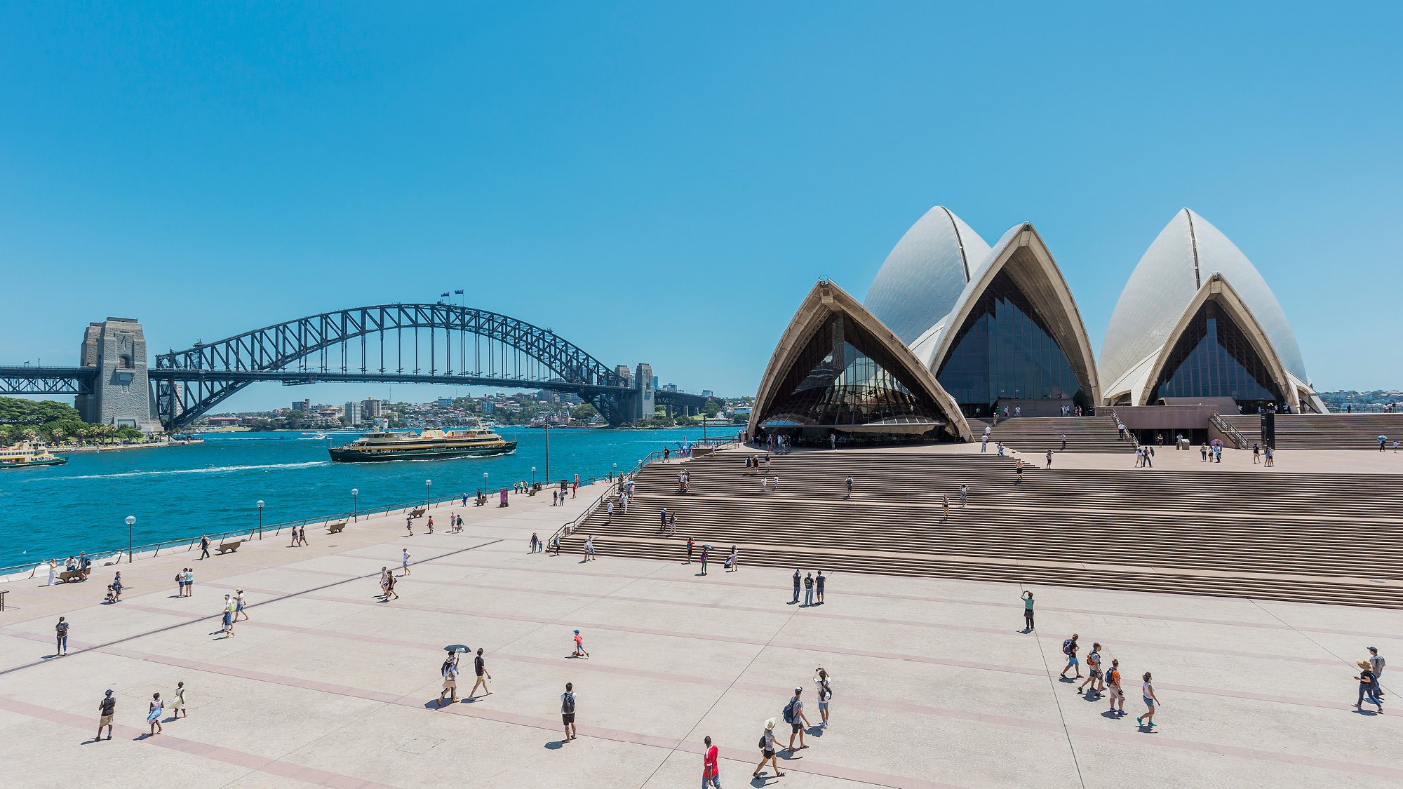 Wide angle view of the forecourt of the Sydney Opera House with people walking around