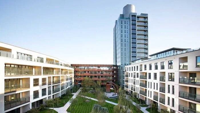 Apartment buildings surrounding a courtyard garden, with a tower on the right hand side.
