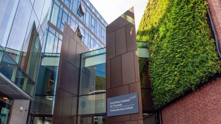 Building with a sign saying Trinity Business School and the Irish translation, as well as a wall covered in plants.