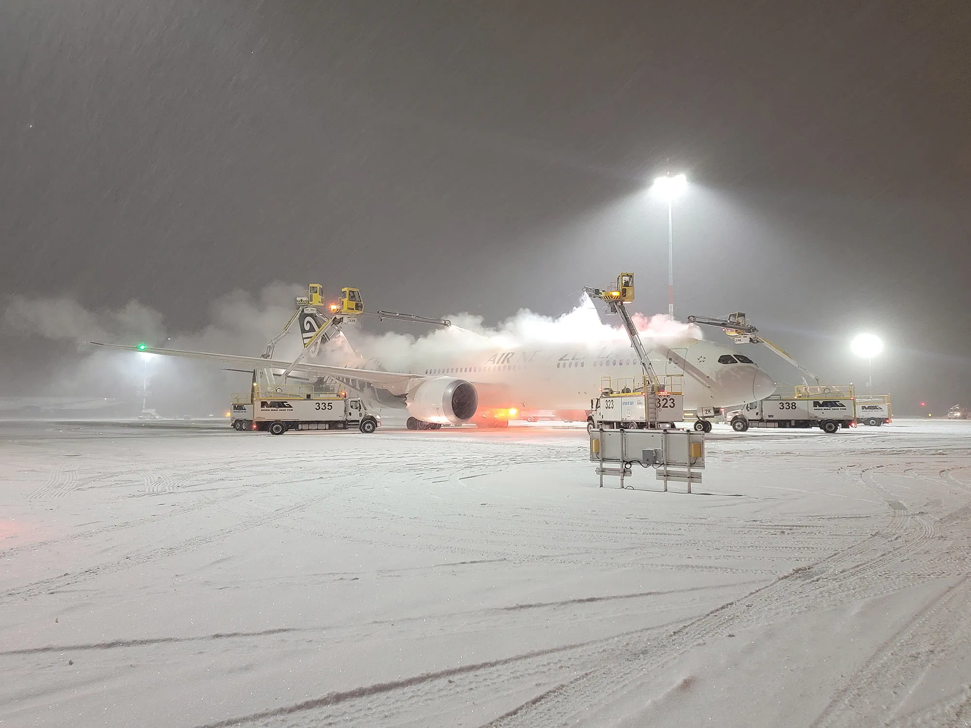 A large white airplane being maintained on the ground during a heavy snowstorm