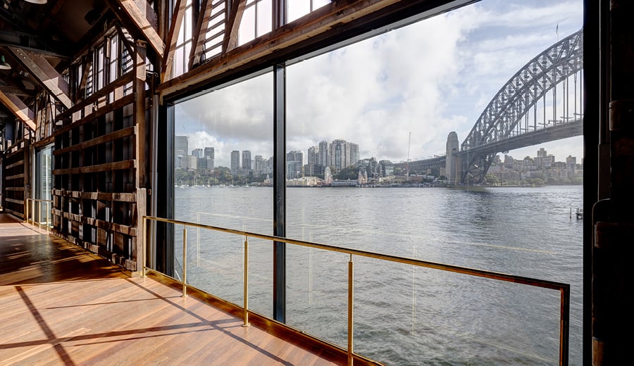 Inside a restored timber and steel building at Walsh Bay Arts Precinct with a view of the Sydney Harbour Bridge through the windows.