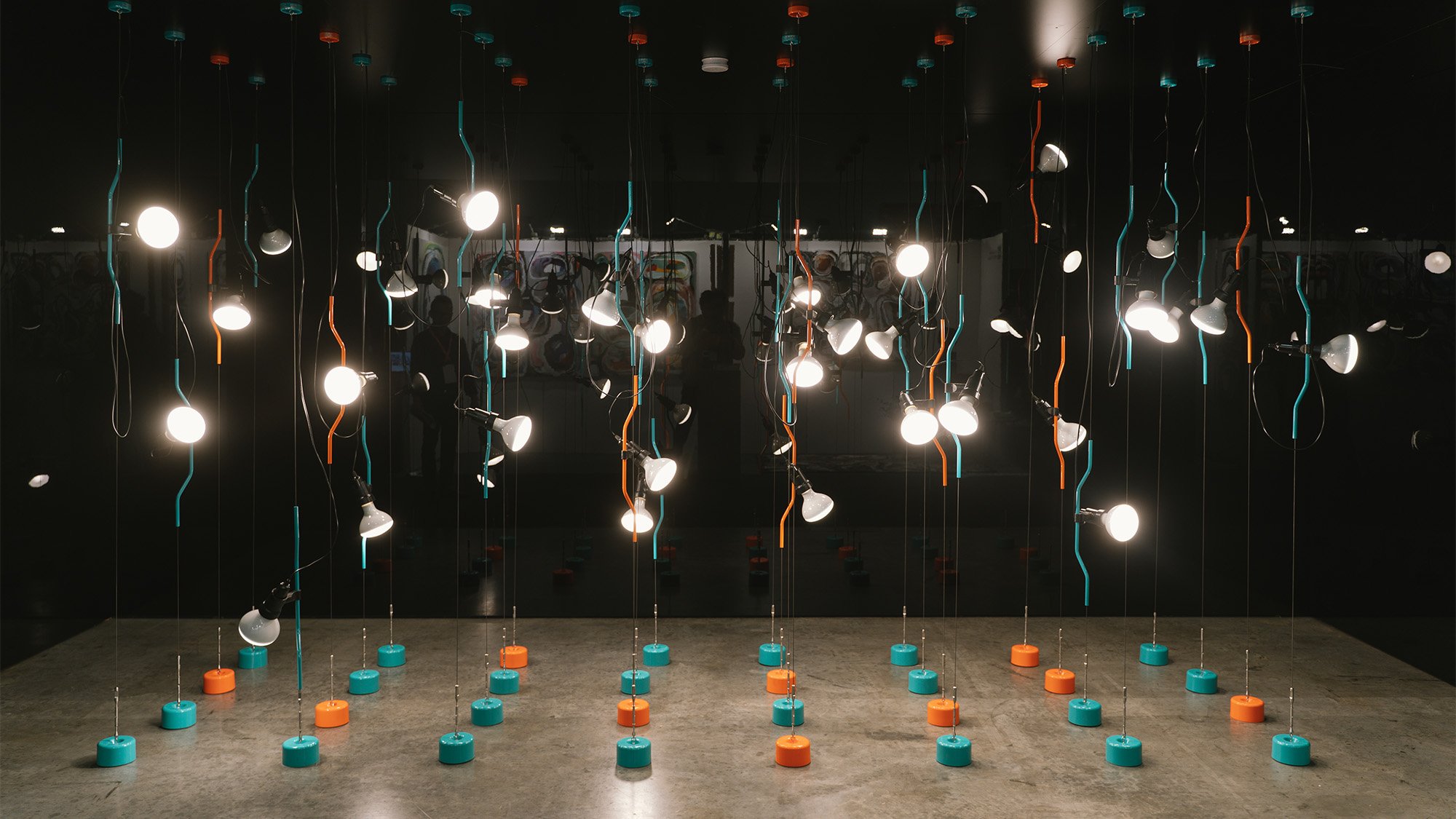 An installation of hanging light bulbs with coloured round plastic discs laid on the timber floor. 