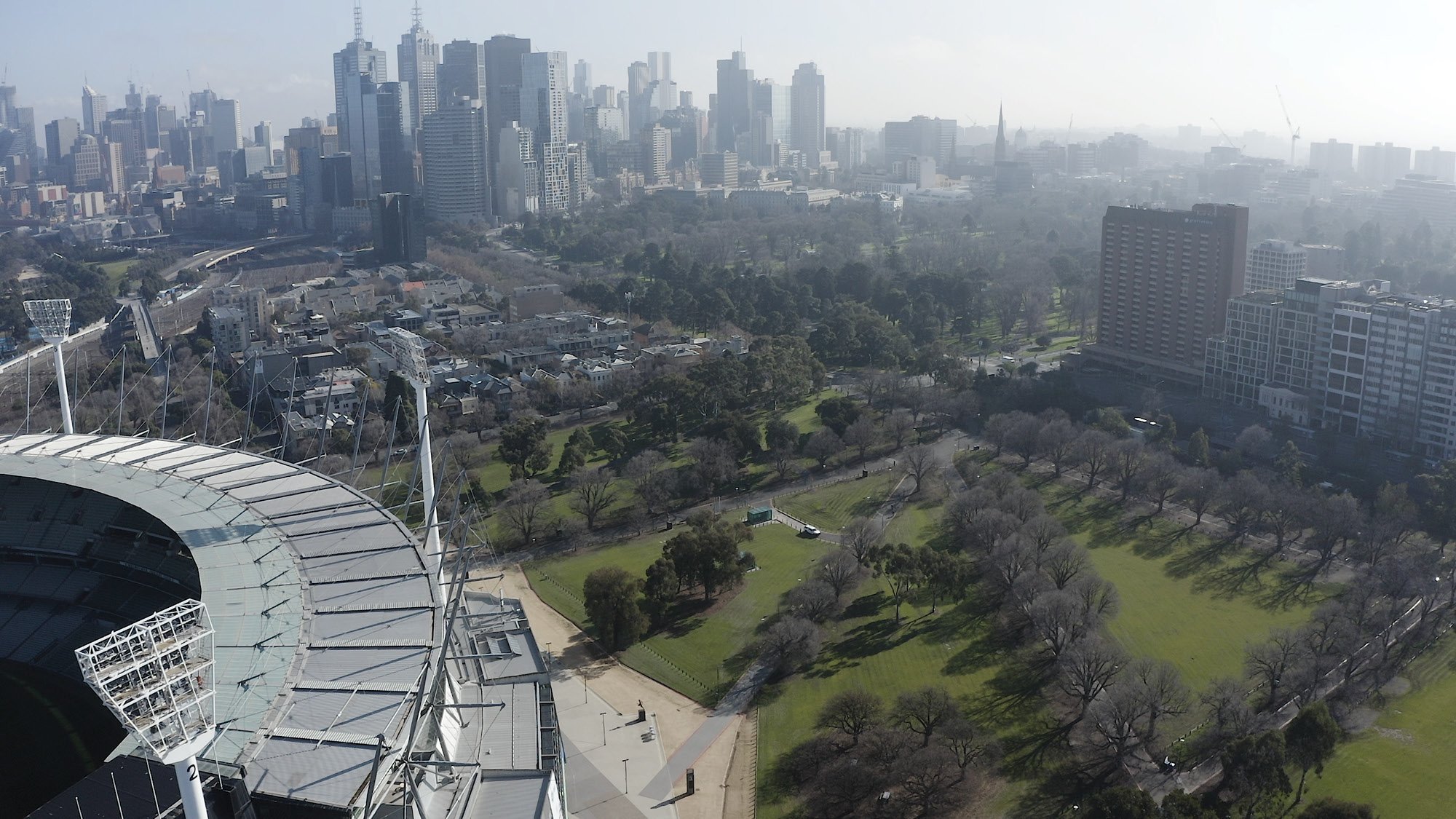Aerial view over a Melbourne city with a grass field with two glass buildings in the foreground