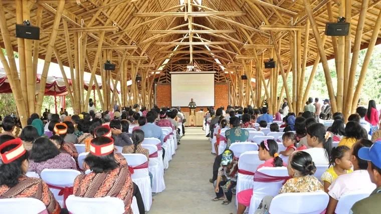 A group of people sitting inside a community centre constructed from bamboo