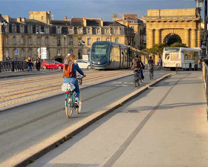 People cycling across a bridge with a tram and a bus visible