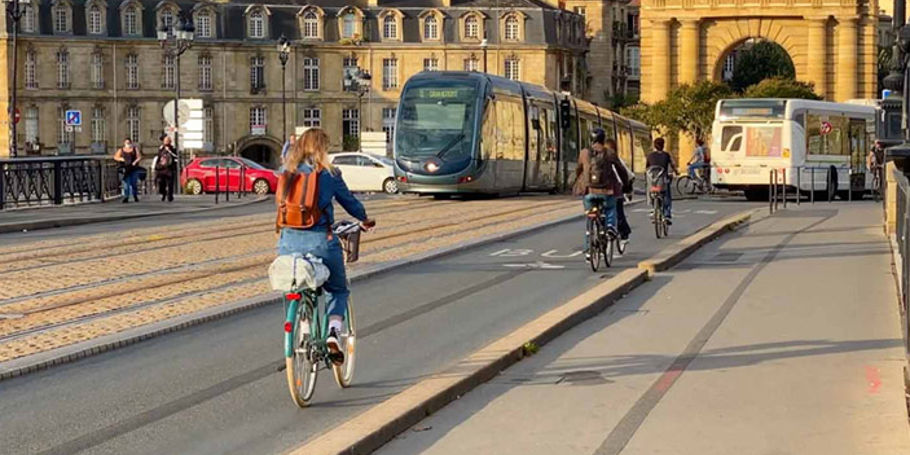 People cycling across a bridge with a tram and a bus visible