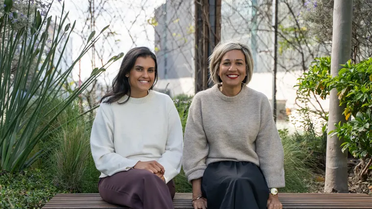 A couple of women sitting on a bench smiling at camera