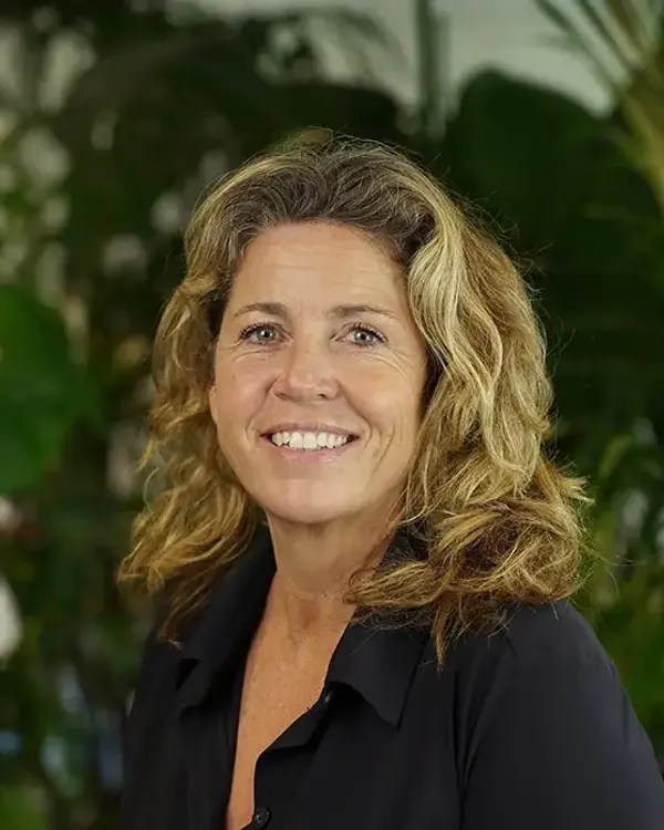 A person smiling in front of a bush.