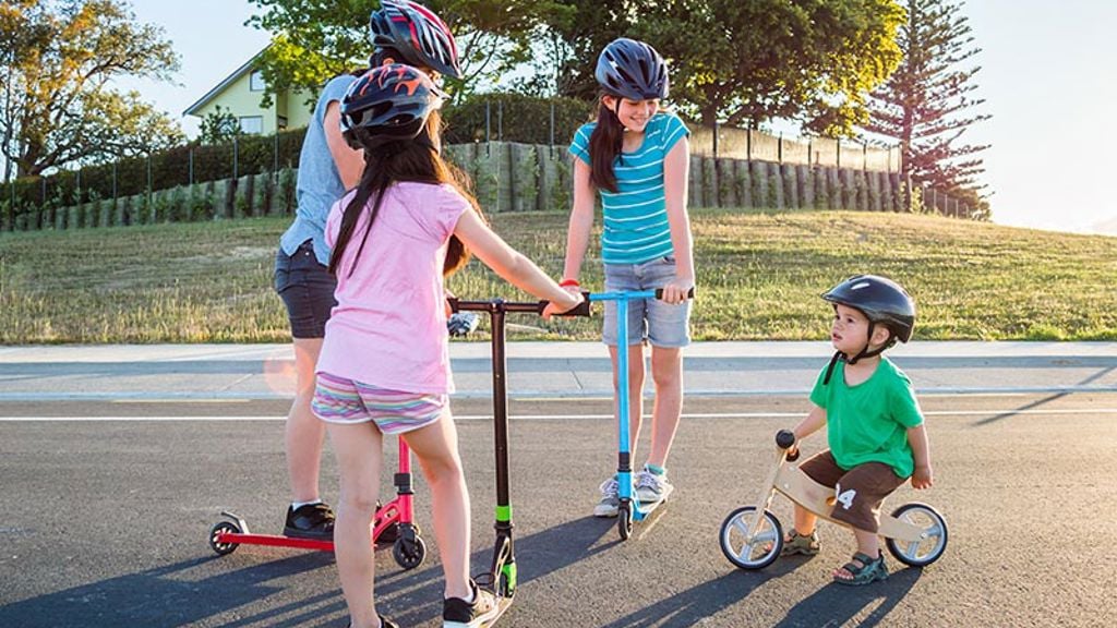 A group of children with scooters and bikes talking on a sunny day