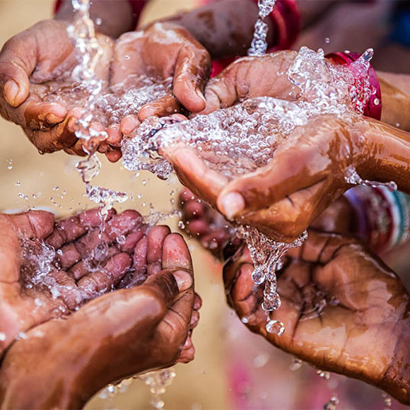 A group of hands cupping water flowing from a tap