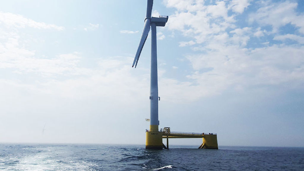 A large white windmill in the middle of the ocean.