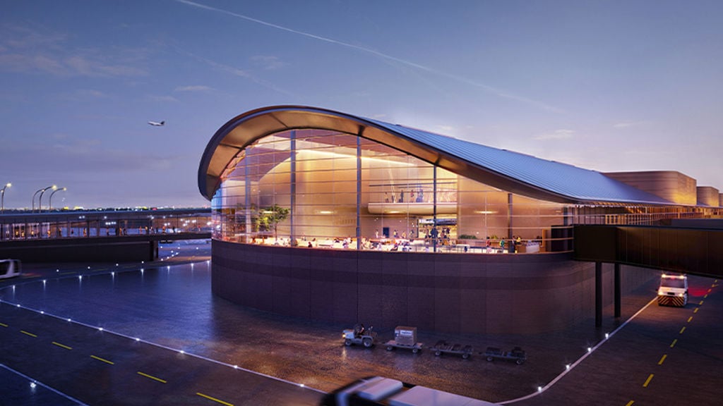 An airport terminal building with a curved roof and large glass facade at dusk