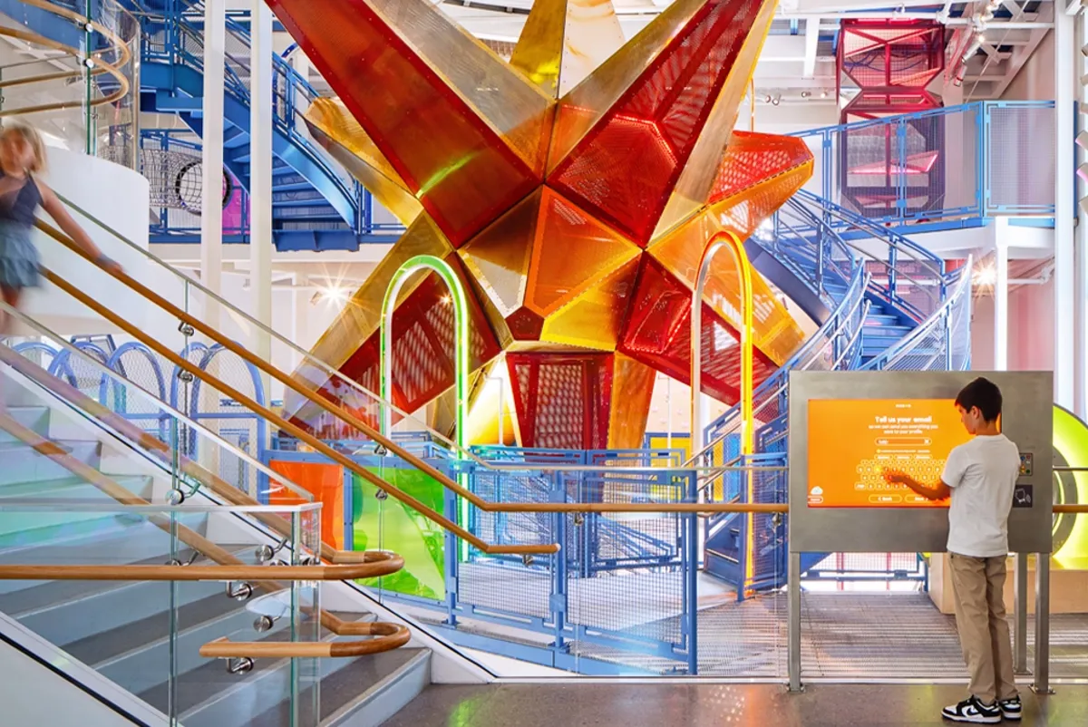 The interior of a colorful atrium with a starburst-like interactive climber, that is orange and red.