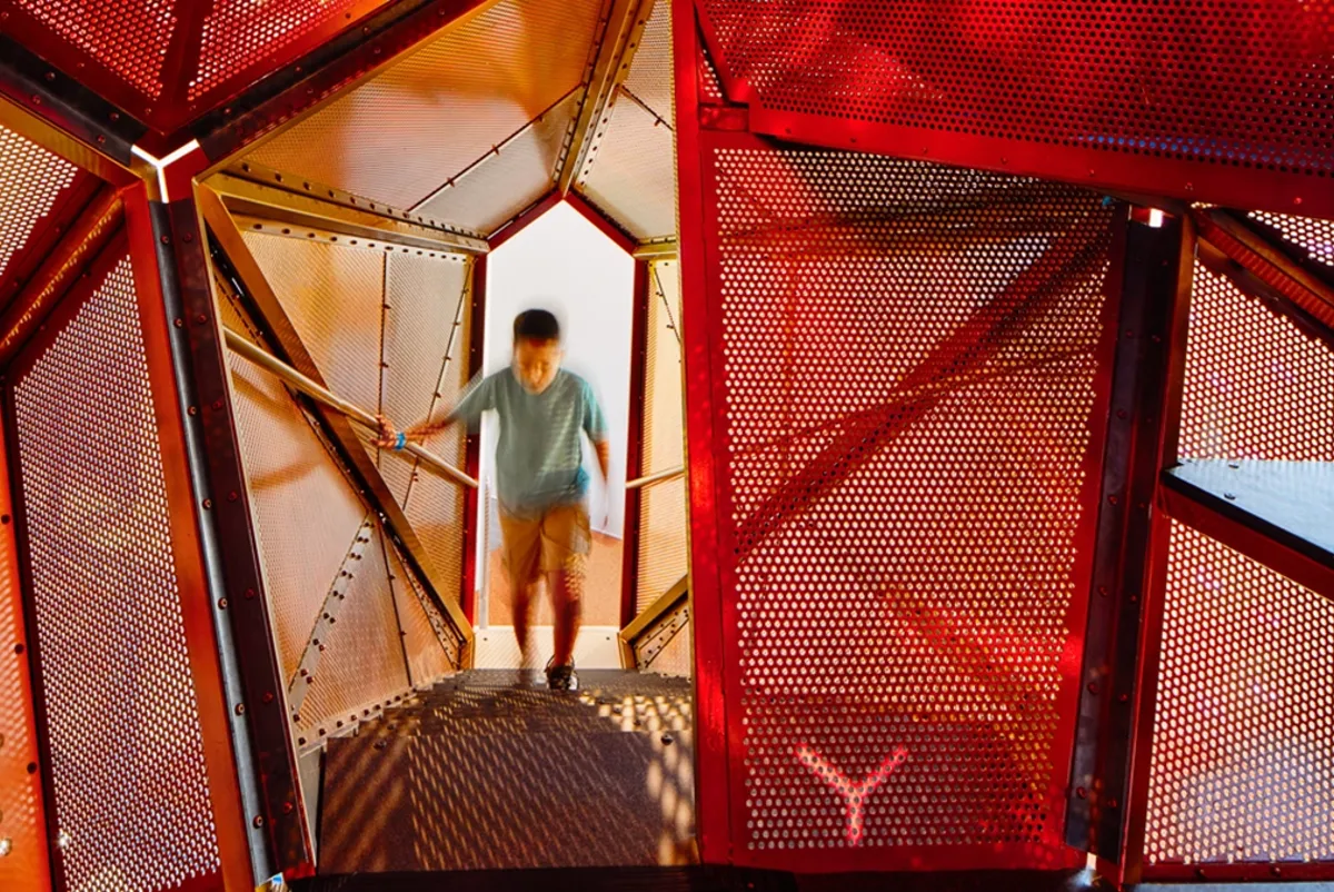 A small child walking into the interior of a starburst-shaped climber, it is orange and red inside.