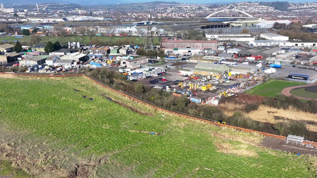 A large green field with buildings and trees in the background.