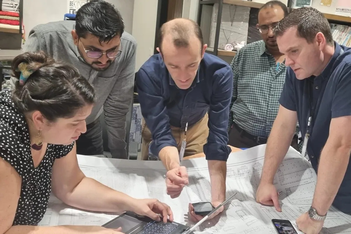 A group of people looking at a laptop, drawings and inspection results on a phone.