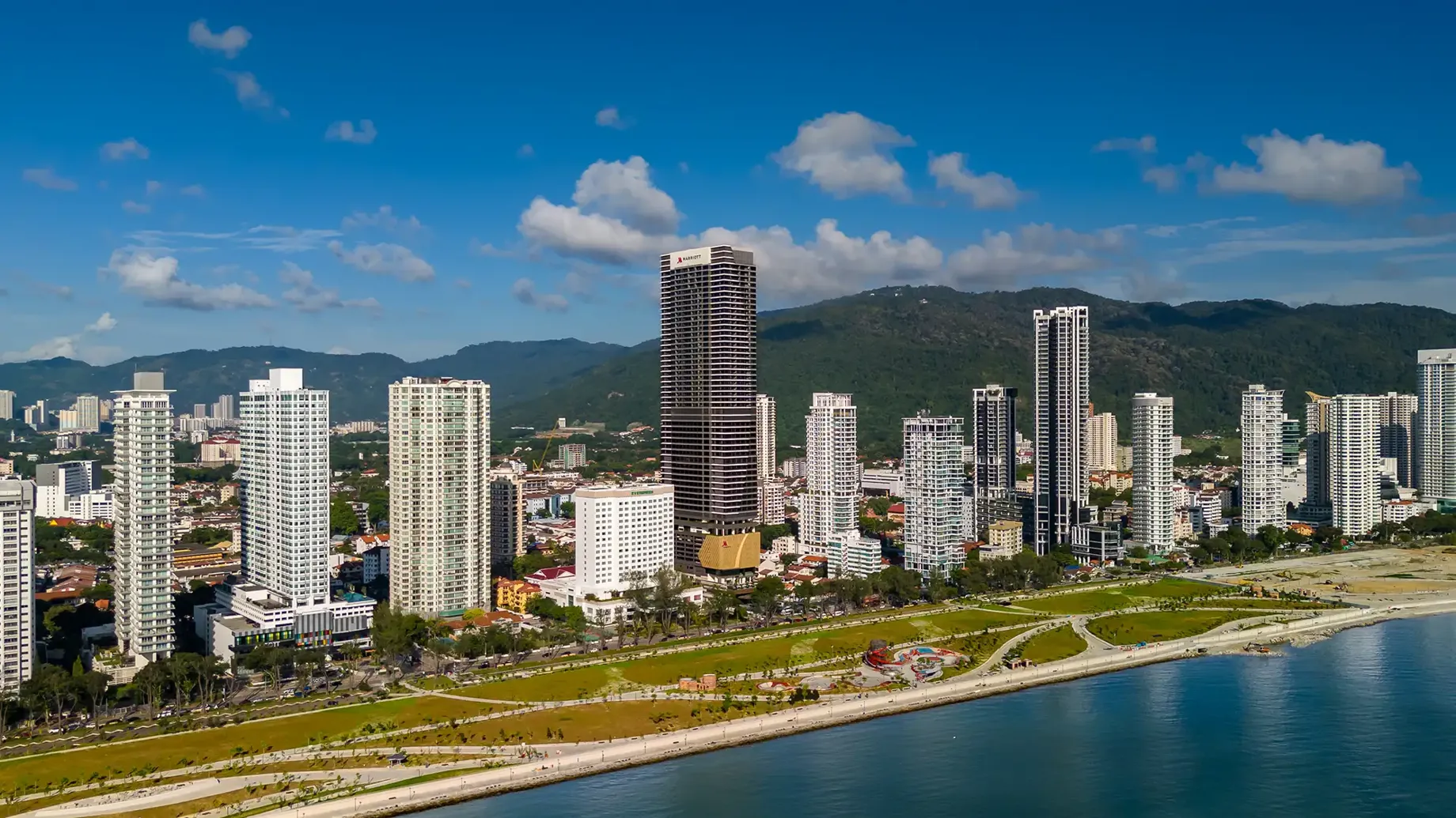 A skyline of tall buildings on the Penang waterfront with mountains behind