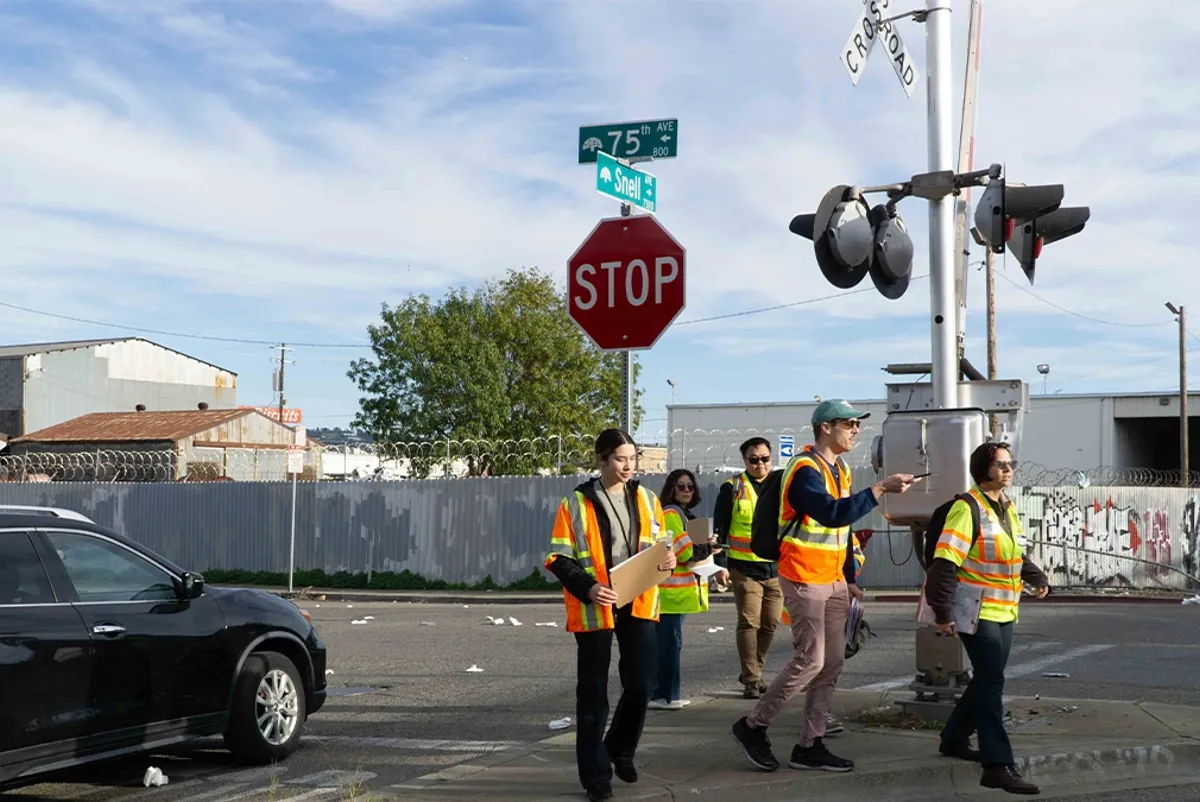 A group of people in safety vests crossing the street next to a stop sign and railroad crossing